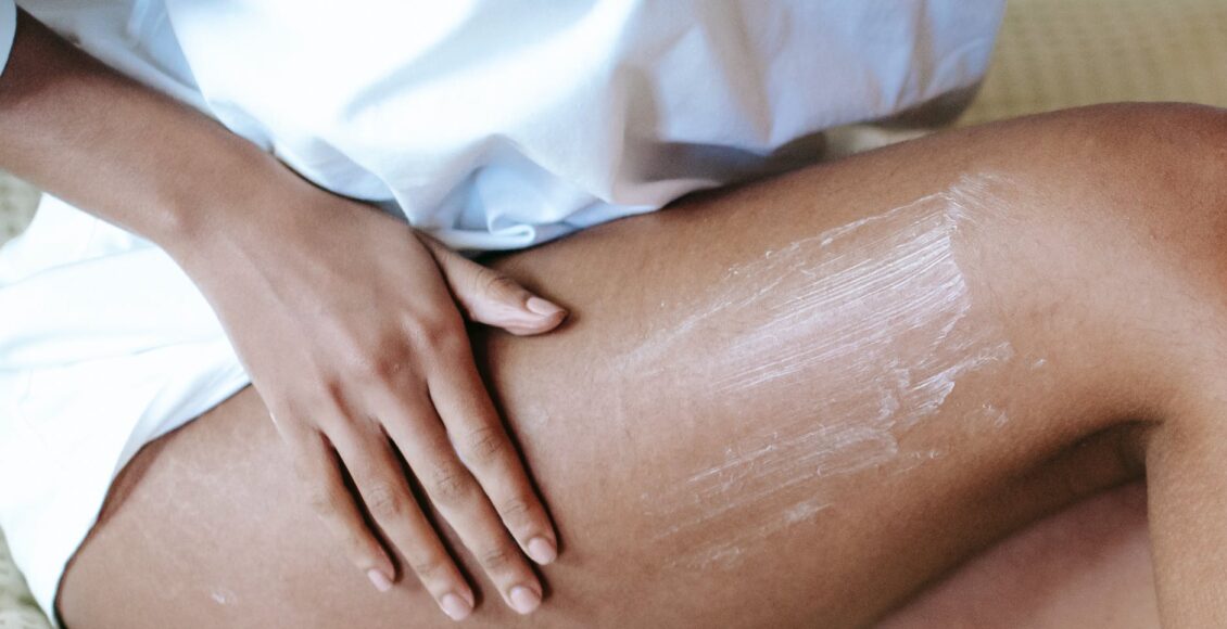 woman massaging leg with lotion in bedroom